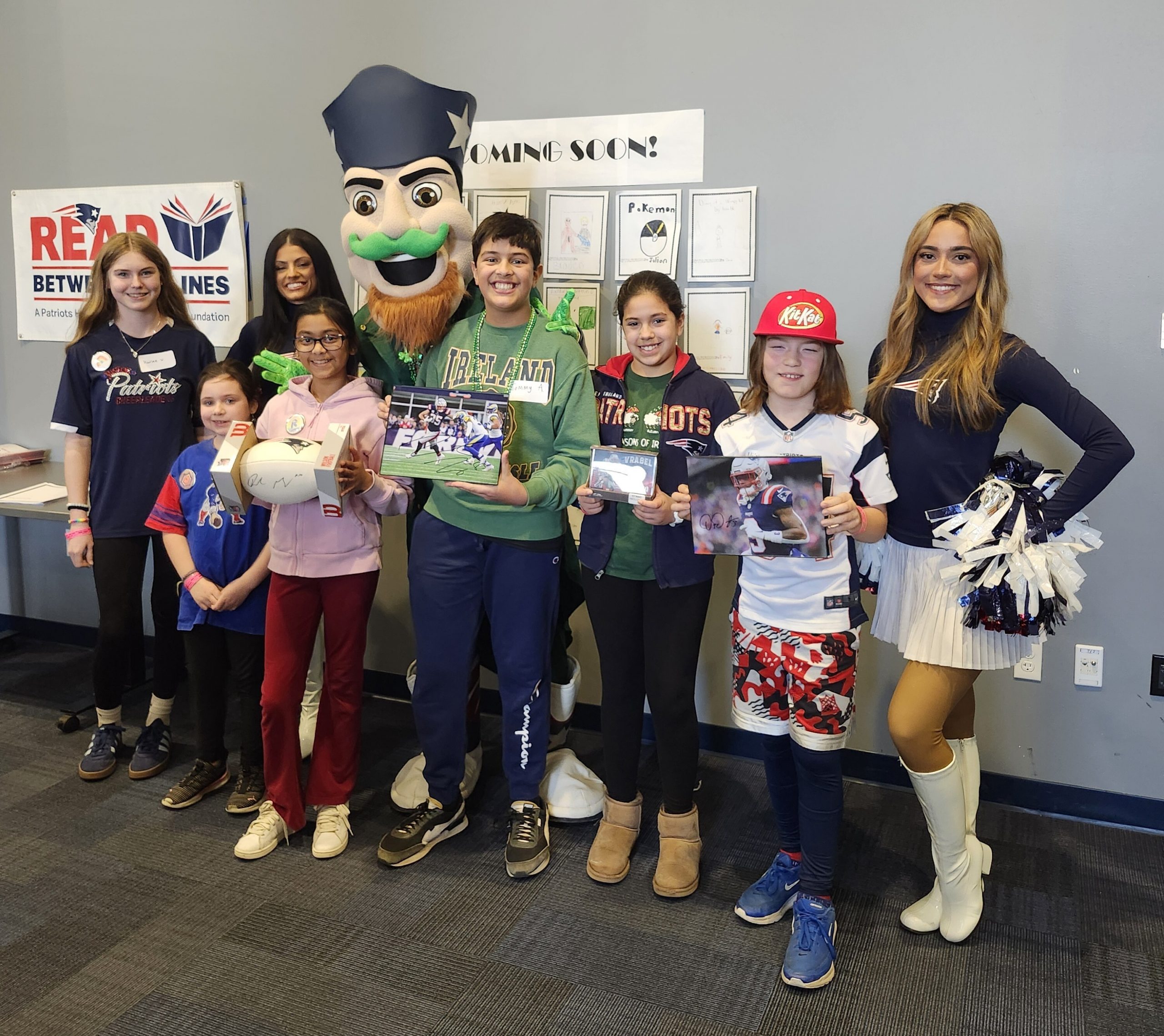 Smiling students pose with their challenge prizes standing with Patriots cheerleaders and mascot